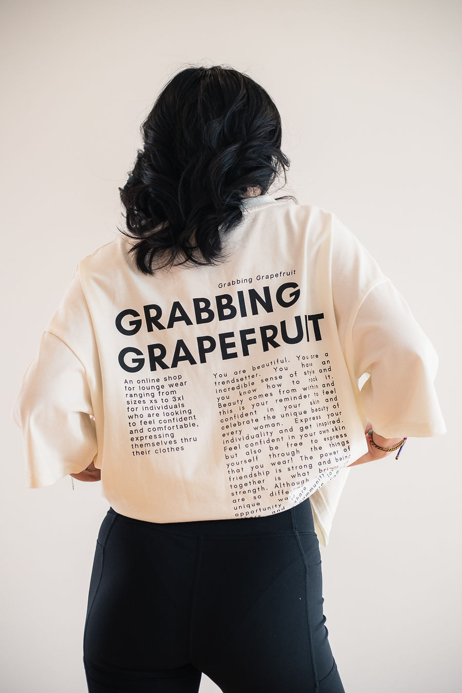 A model with long brown wavy hair looks into the camera with a subtle gaze wearing a Grabbing Grapefruit embroidered, oversized white tee