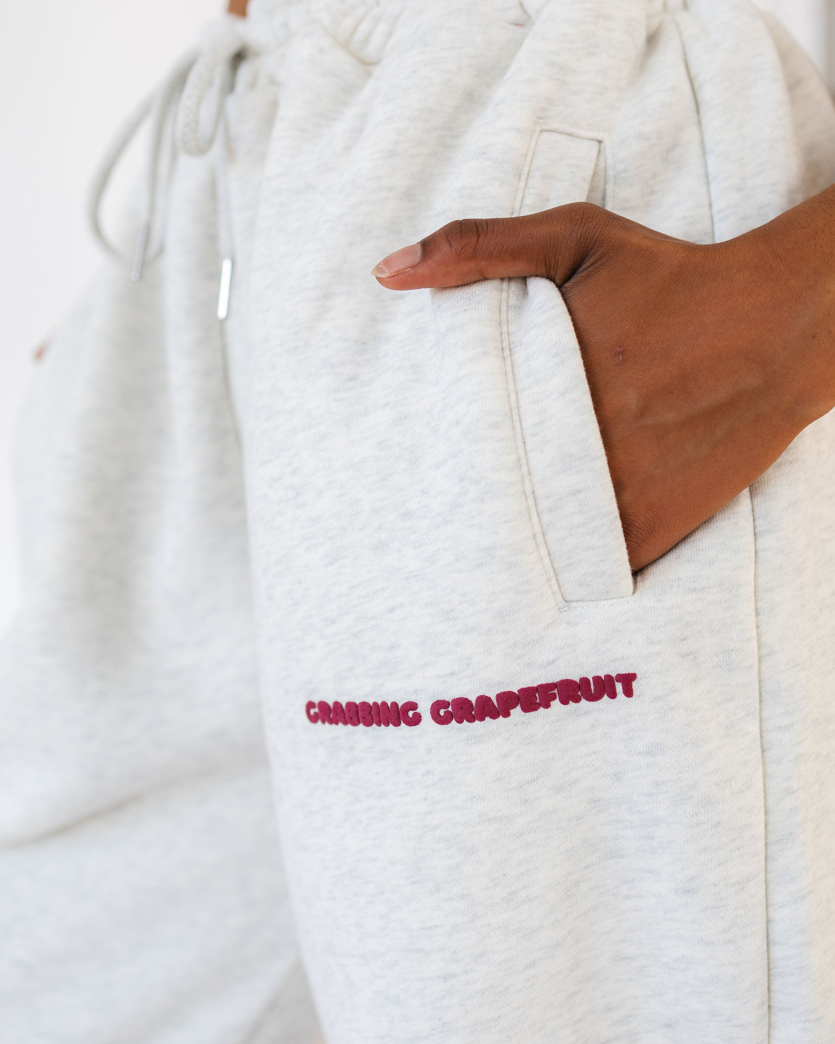 Image of a model from behind from the shoulders down to show Grabbing Grapefruit sweatpants in the colour of Mossi Pine green. Paired with white sneakers and the Grabbing Grapefruit tote bag, the image represents the Sweatsuits collection.